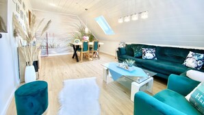 Uma sala de estar moderna com um sofá verde, uma mesa de centro e uma área de jantar com mesa e cadeiras.