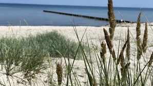 A beach with sand dunes and grass in the foreground, and a calm sea in the background. - Ferienwohnung Poeler Koje (Insel Poel)
