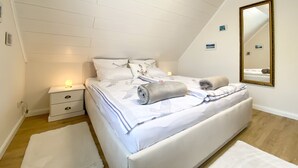 Quarto com cama branca, mesa de cabeceira, espelho e parede branca.