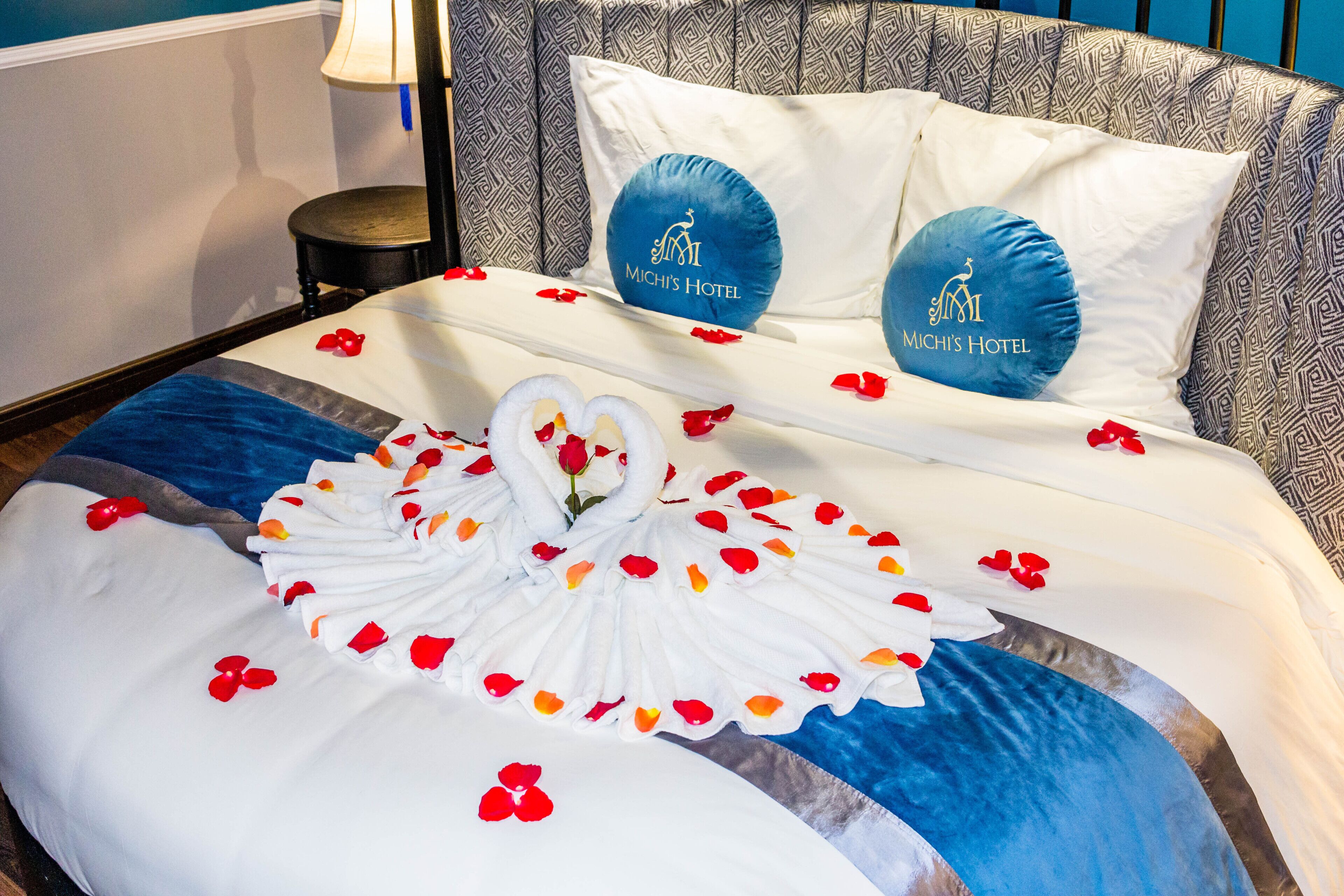 Una cama bien hecha con un diseño de cisne, pétalos de rosa y almohadas con el logotipo del hotel.