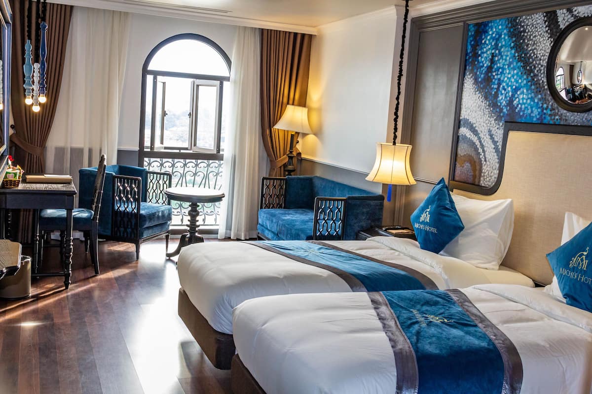 A hotel room with two beds, a desk, and a balcony.