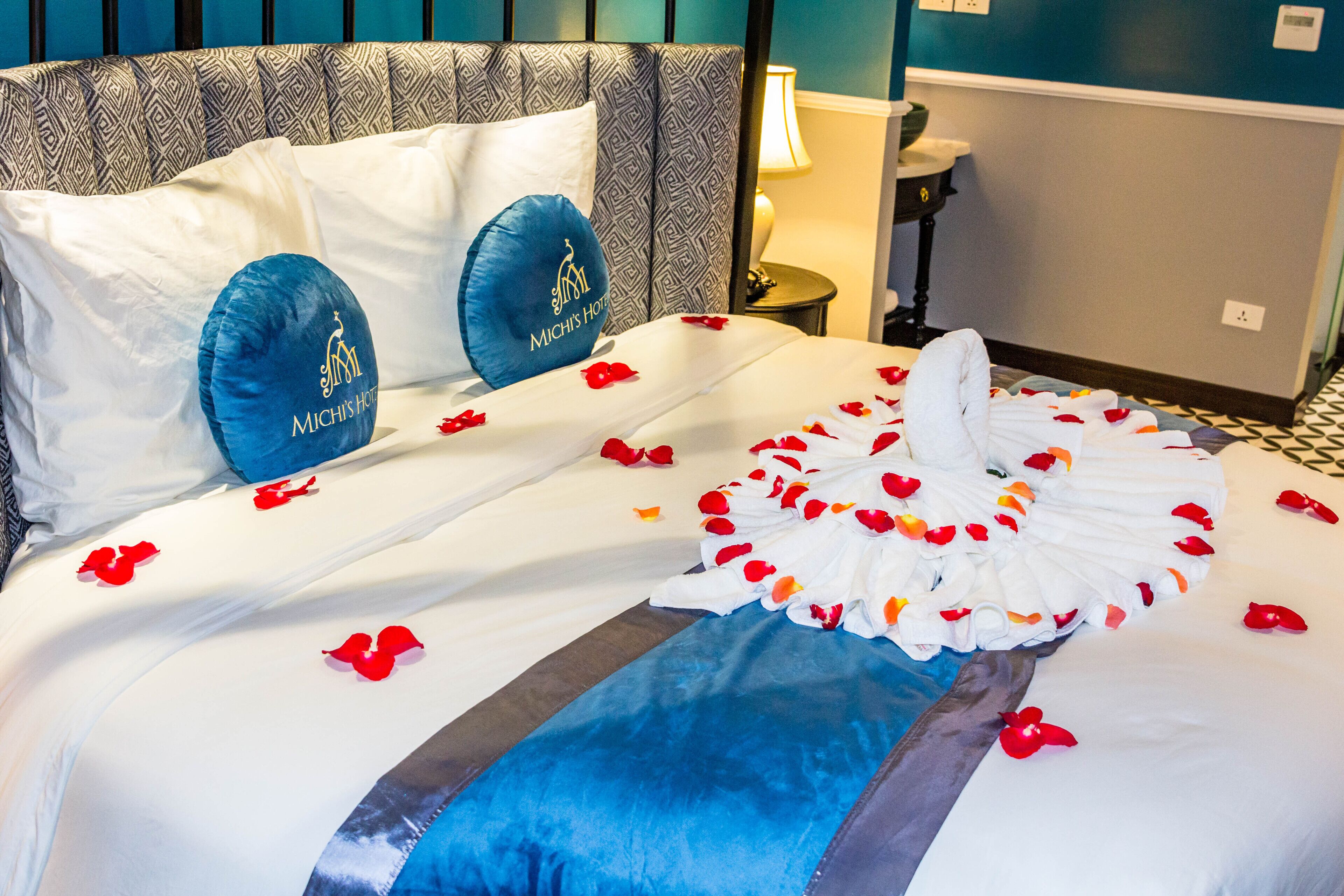 Habitación de hotel con una cama bien hecha, cabecera con diseño geométrico y almohada con el logotipo del hotel.