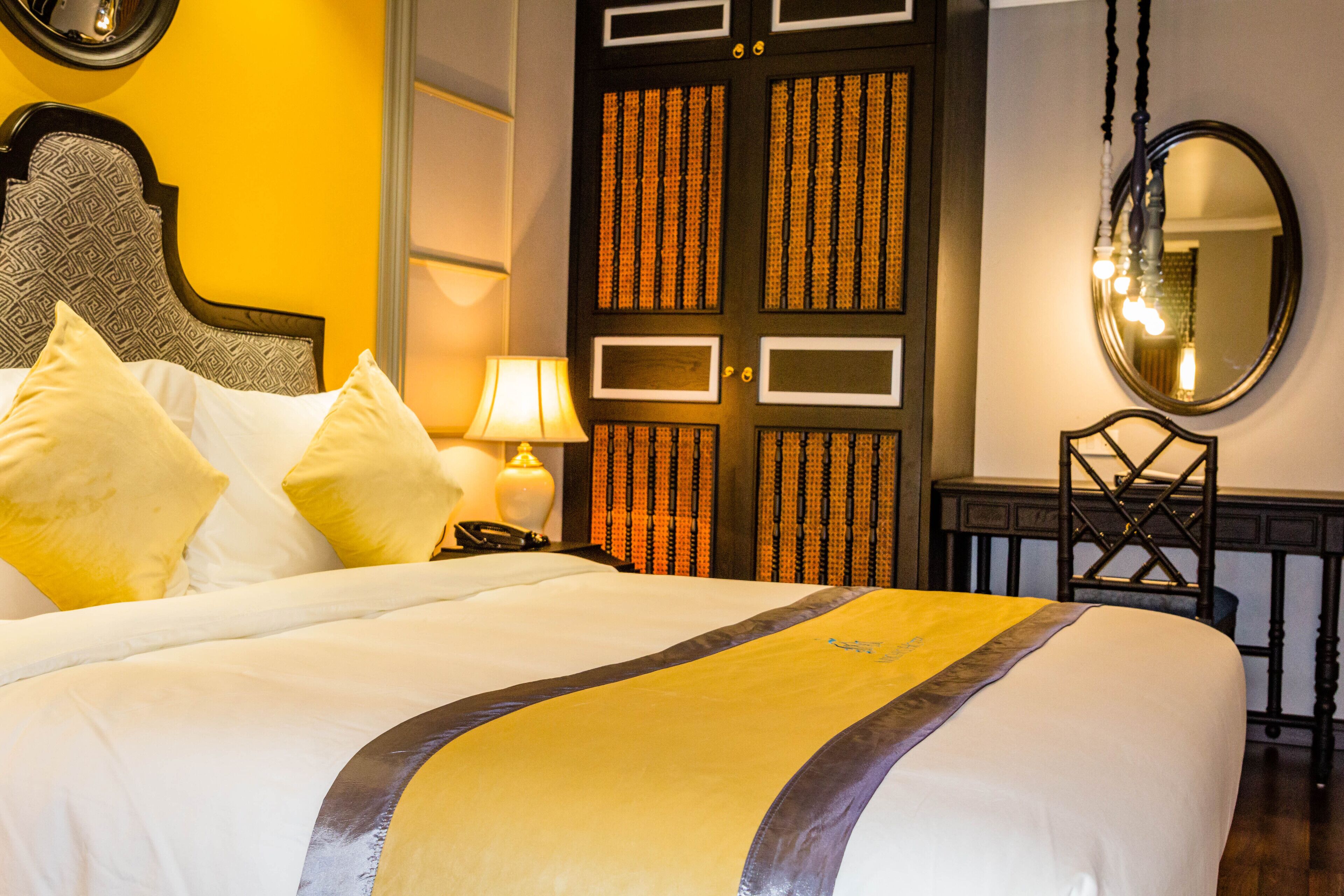 A hotel room with a bed, a nightstand, a lamp, a chair, a mirror, and a wardrobe.
