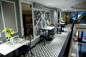 Un restaurante con piso estampado, sillas blancas y negras, y una pared decorativa con motivos florales.