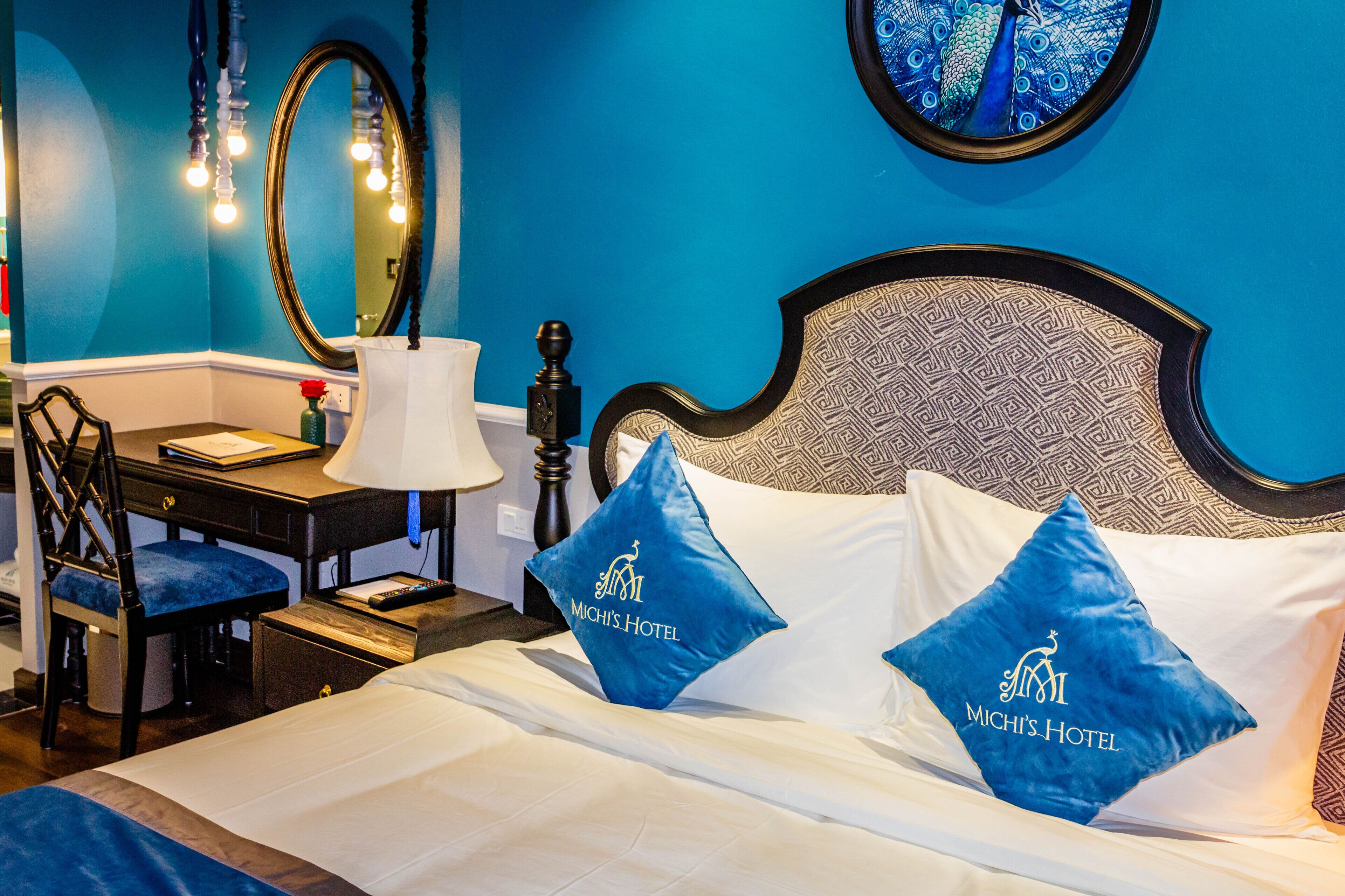 A hotel room with a bed, a desk, and a chair. The bed has two pillows with the hotel's logo.