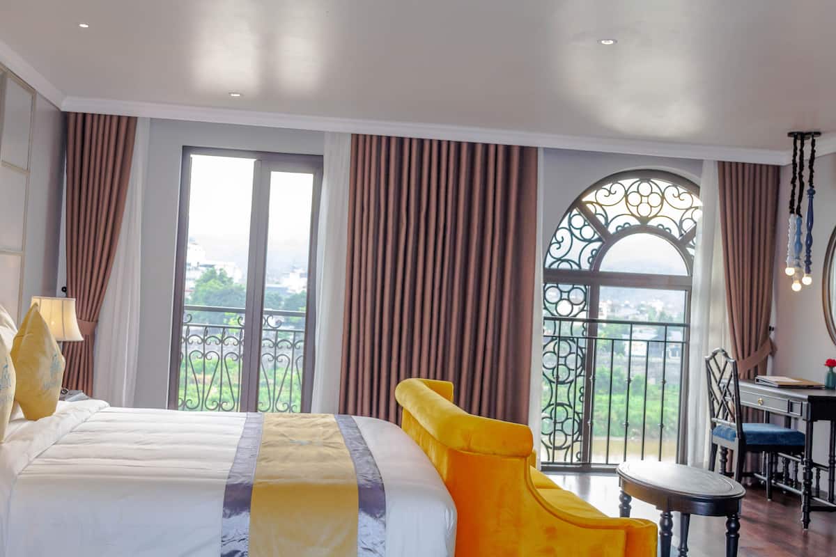 A hotel room with a large bed, a desk, and a view of greenery through a window.