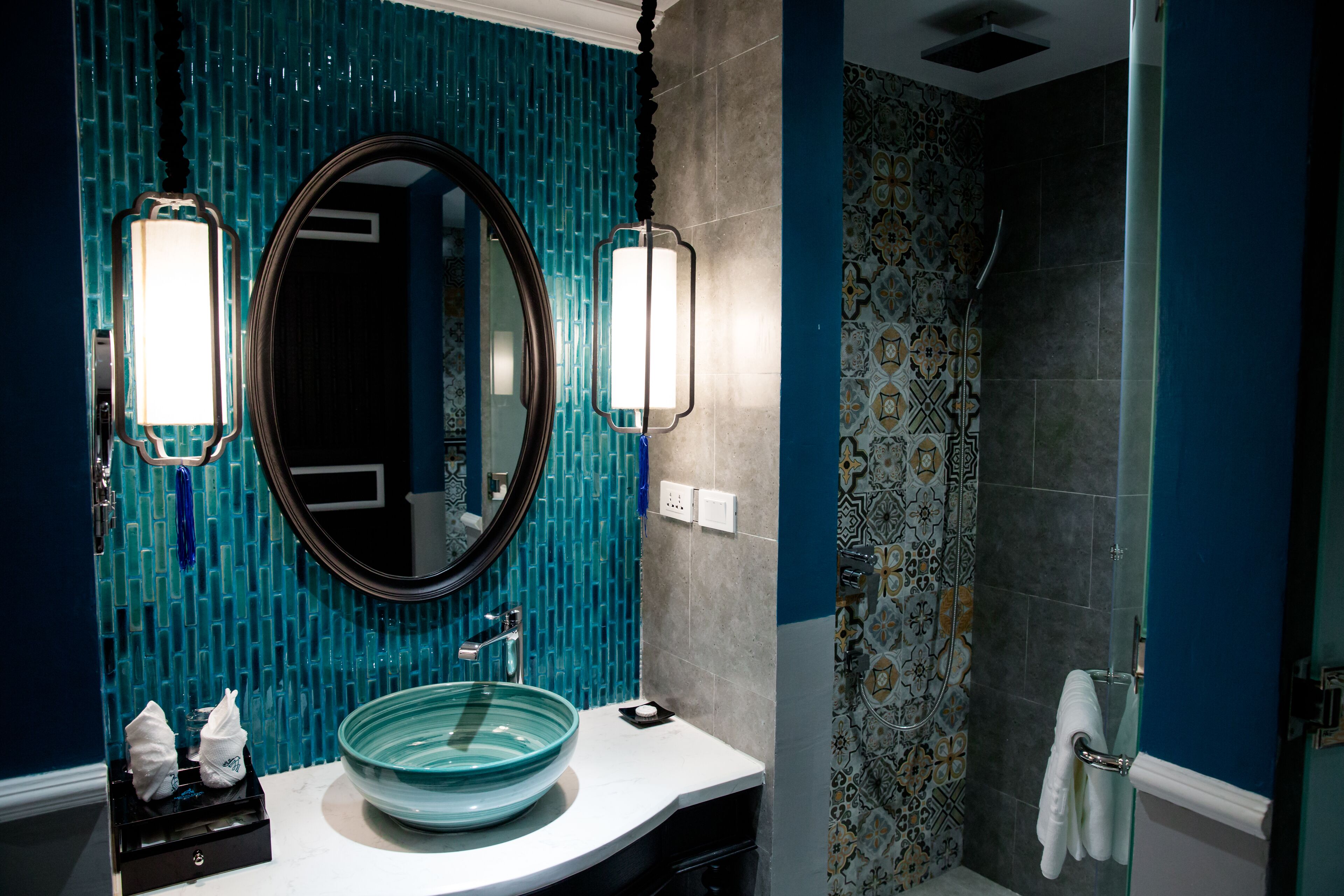 A bathroom with a large mirror, a bowl sink, and a shower with patterned tiles.
