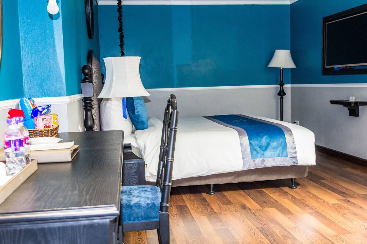 A hotel room with a bed, a desk, a chair, a lamp, and a TV.