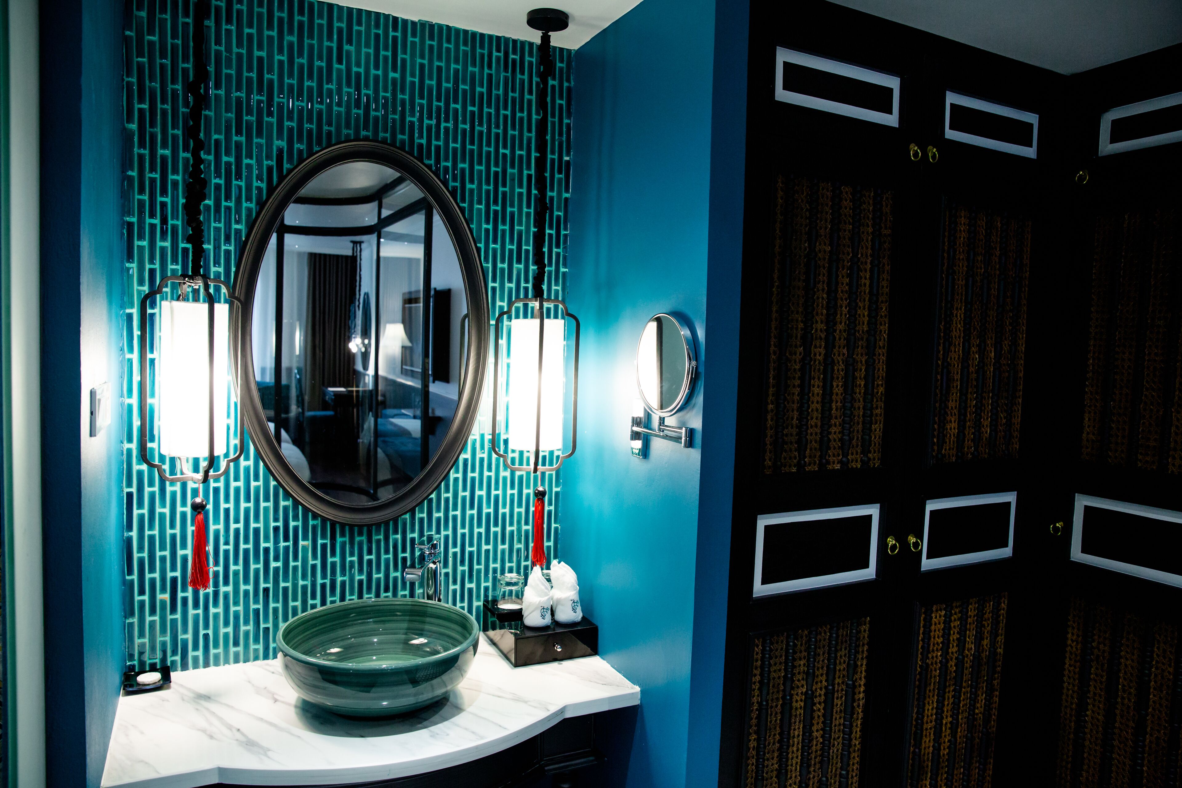 Un baño con un espejo redondo grande, dos luces empotradas en la pared, un lavabo de mármol y una pared de azulejos azules.