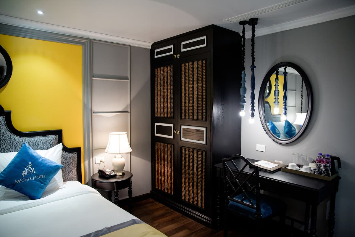 A hotel room with a bed, a desk, a wardrobe, a mirror, and a lamp.