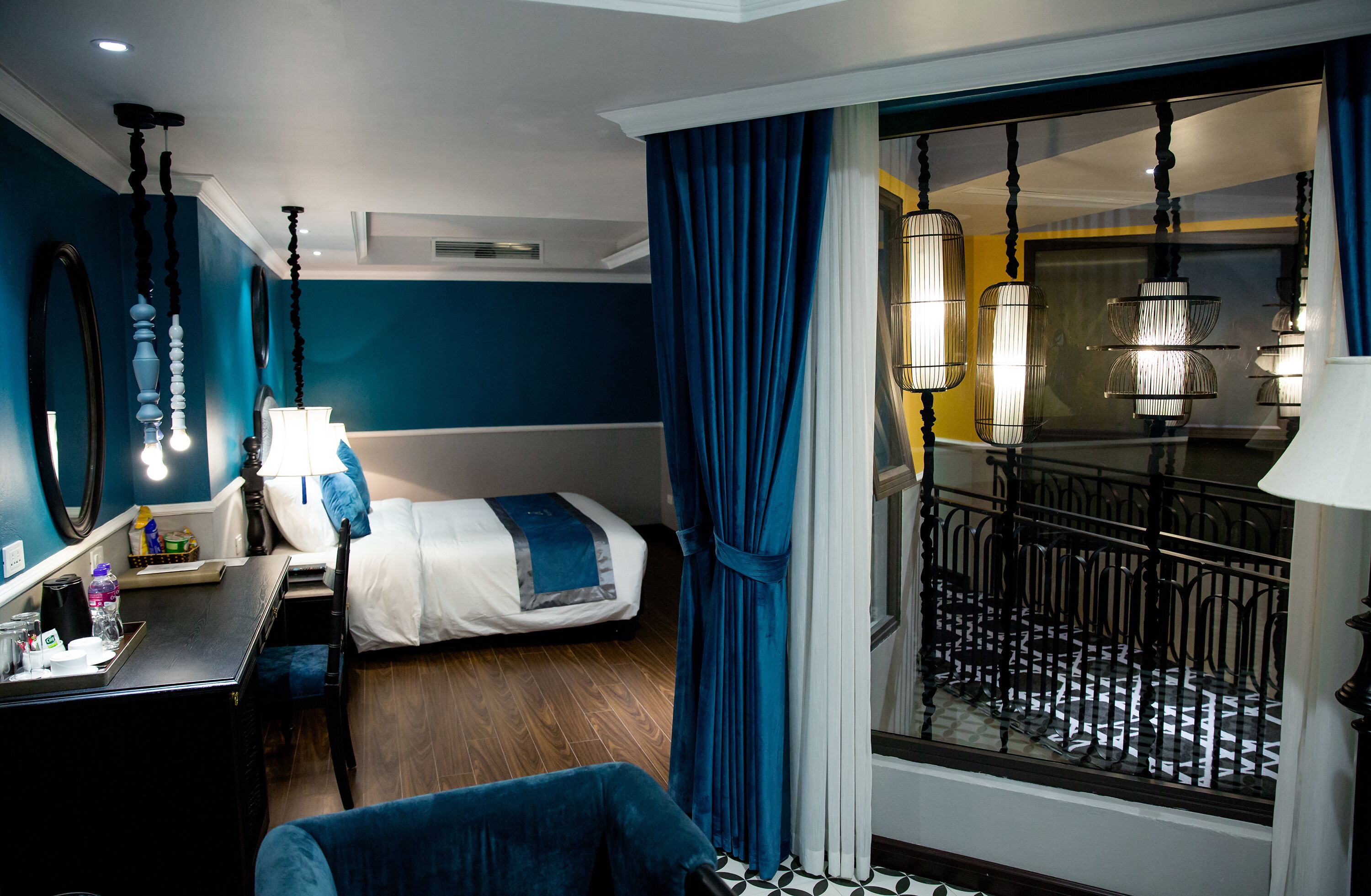 A hotel room with a bed, a desk, a chair, a mirror, and a view of a balcony with railings.