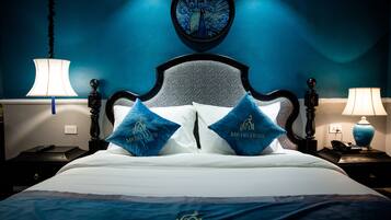 A bed with a headboard, two pillows with a logo, a wall clock, and two bedside tables with lamps.