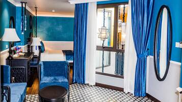 A hotel room with a blue and white color scheme, a bed, a desk with a lamp, a chair, and a patterned floor.