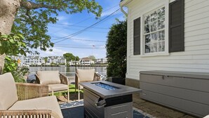 Een terras met buitenmeubilair, een barbecue en uitzicht op een meer en gebouwen op de achtergrond.