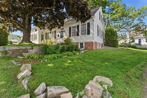 A two-story house with a front porch, a brick foundation, and a well-maintained lawn with rocks and shrubs.