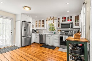 A modern kitchen with white cabinetry, stainless steel appliances, and a wooden floor.