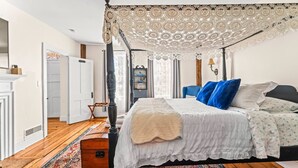 Een hemelbed met een kantborduursel, een houten dressoir en een kamerkleed met dessin.