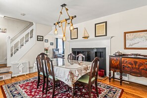 A dining room with a glass table, wooden chairs, a chandelier, a fireplace, and a staircase. - Mystic Riverfront Captain`s Home (Groton)