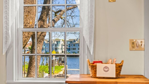 Een kamer met een raam dat uitkijkt op een waterpartij en gebouwen, een houten tafel met een mand, en een stopcontact.