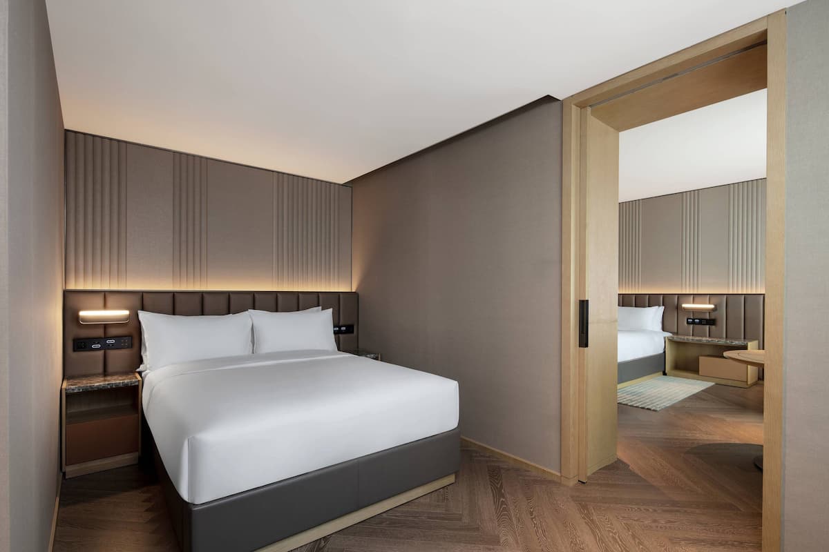 Une chambre d’hôtel moderne avec un grand lit, des tables de chevet, une petite table, un miroir et un plancher en bois.