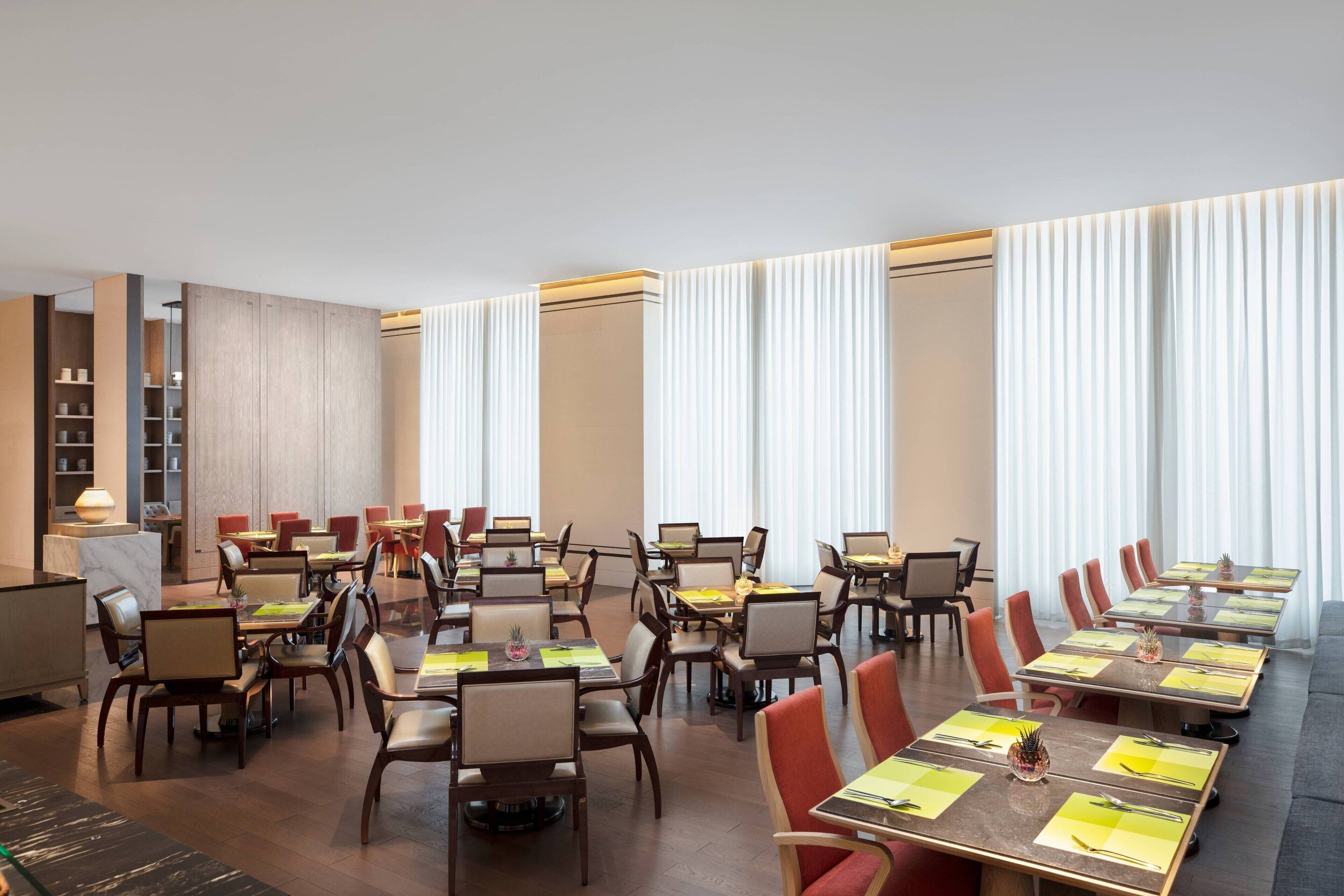 A conference room with multiple tables and chairs, large windows with curtains, and a wooden panel wall.