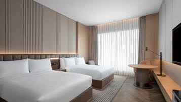 Een moderne hotelkamer met twee bedden, een ronde eettafel, een televisie en een groot raam met gordijnen.