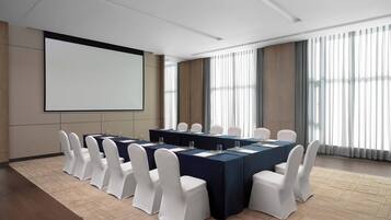Una sala de conferencias con una pantalla grande, varias mesas y sillas blancas.