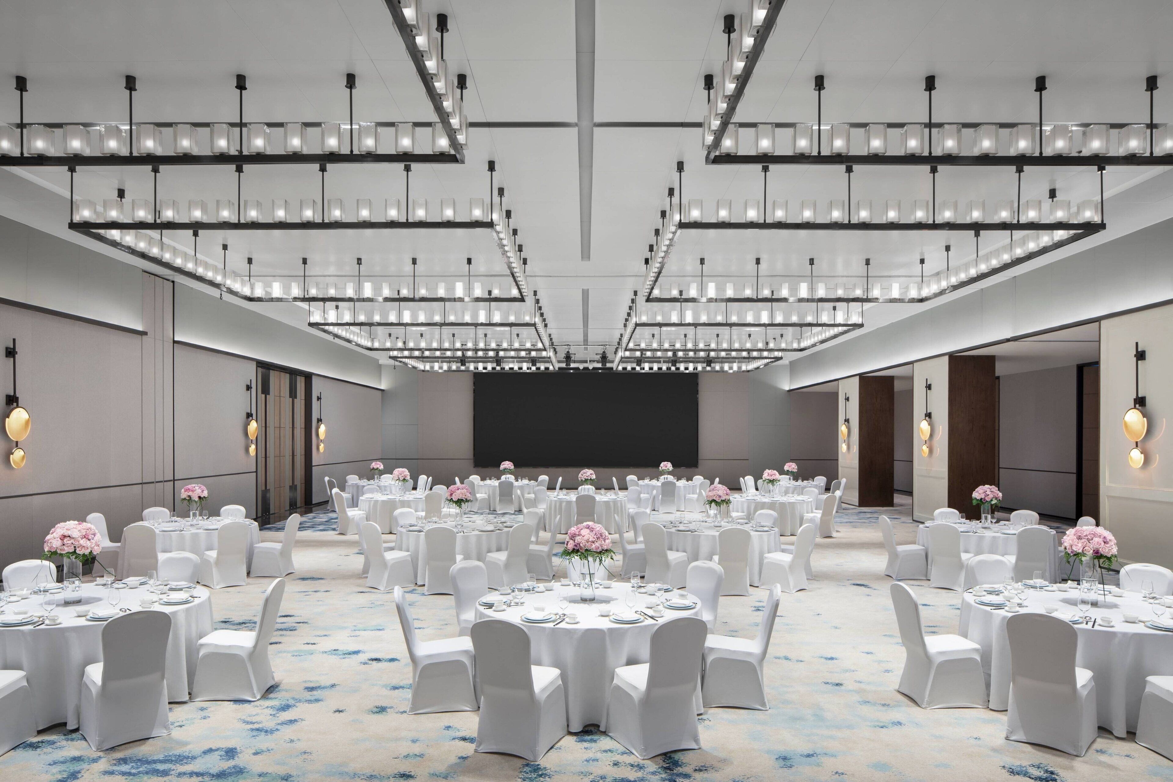 Un amplio salón de conferencias con mesas redondas, sillas blancas y centros de mesa florales.