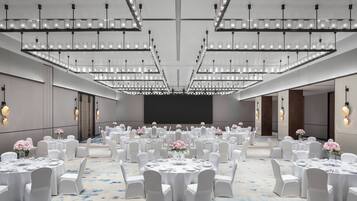 Un amplio salón de conferencias con mesas redondas, sillas blancas y centros de mesa florales.