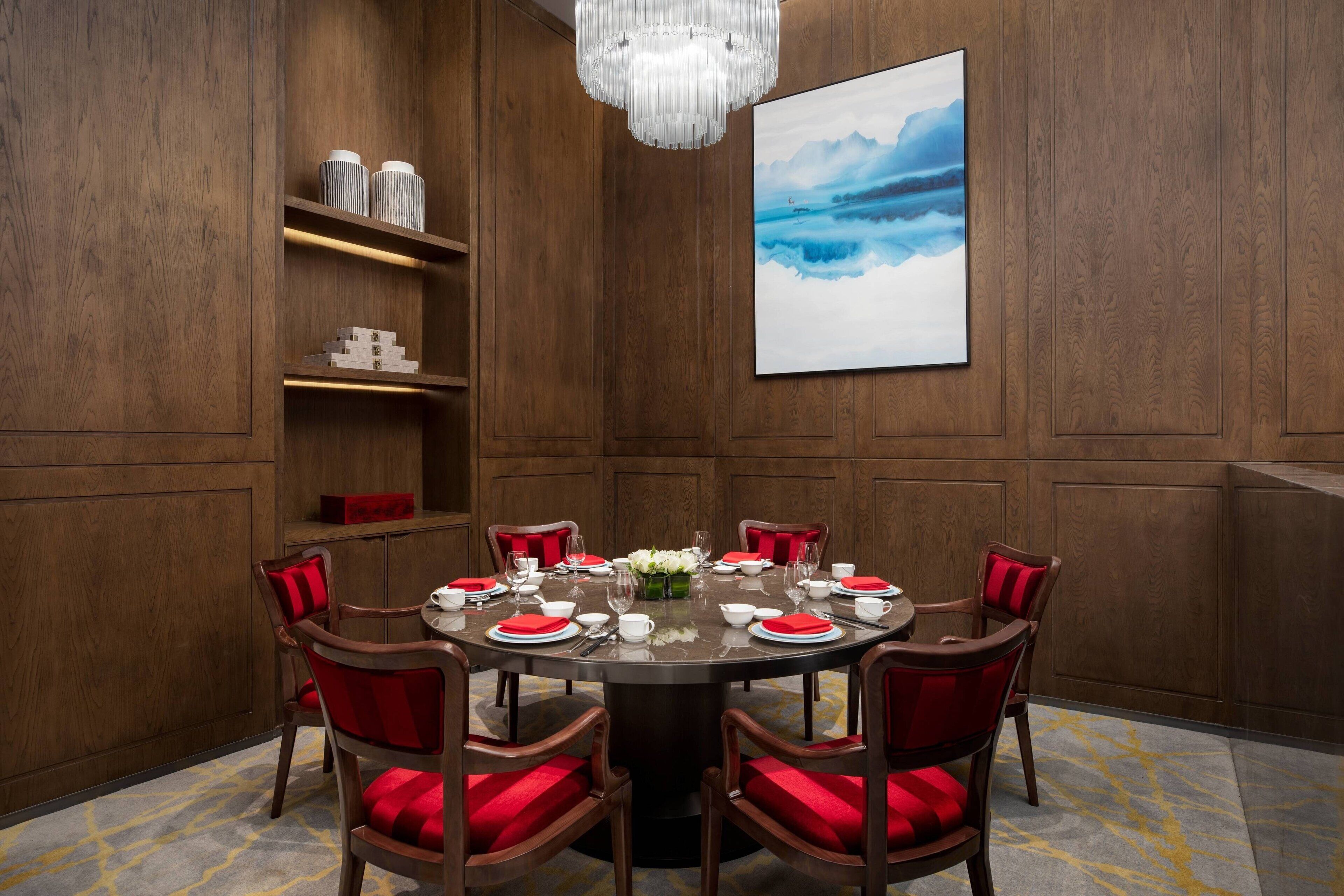 A conference room with a round table, red chairs, and a chandelier.