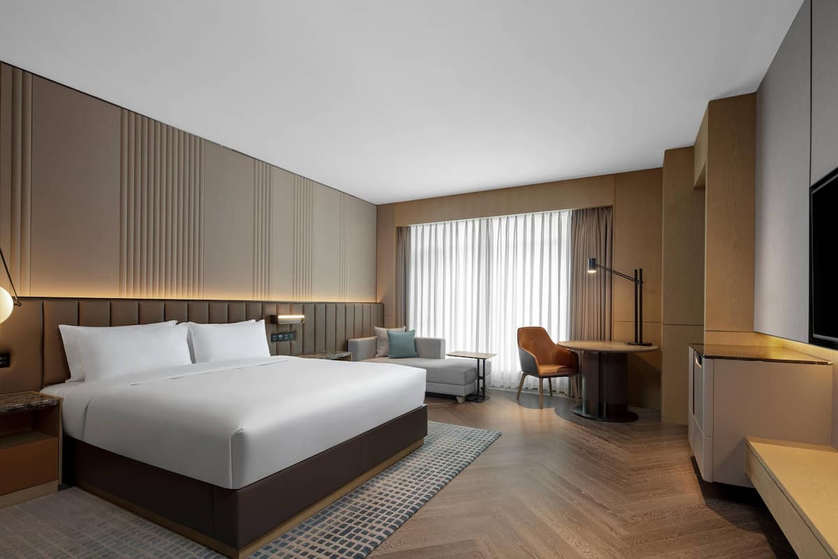 Une chambre d’hôtel moderne équipée d’un grand lit, d’un bureau, d’une chaise, d’une télévision et d’une fenêtre avec des rideaux.
