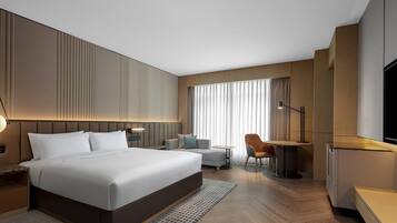 A modern hotel room with a large bed, a desk, a chair, a television, and a window with curtains.