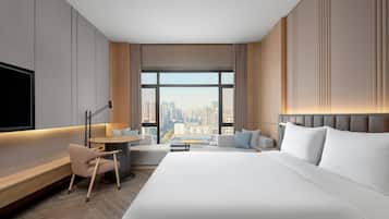 A modern hotel room with a large bed, a desk, a chair, and a TV.