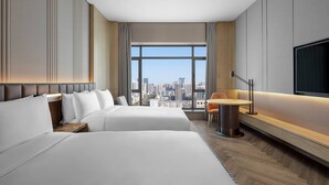 Ein Hotelzimmer mit zwei Betten, Blick auf die Stadt, einem Fernseher und einem kleinen Tisch mit einem Stuhl.