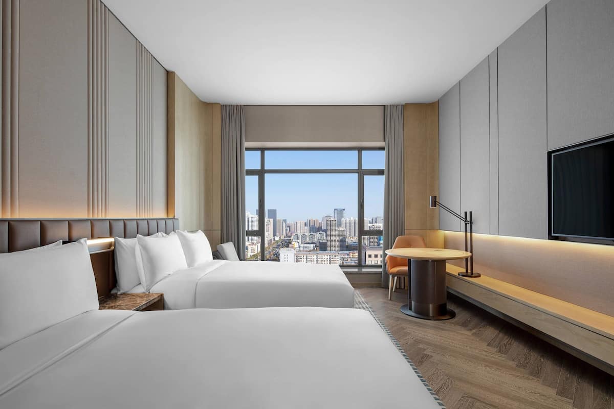 Une chambre d’hôtel avec deux lits, une vue sur la ville, une télévision et une petite table avec une chaise.