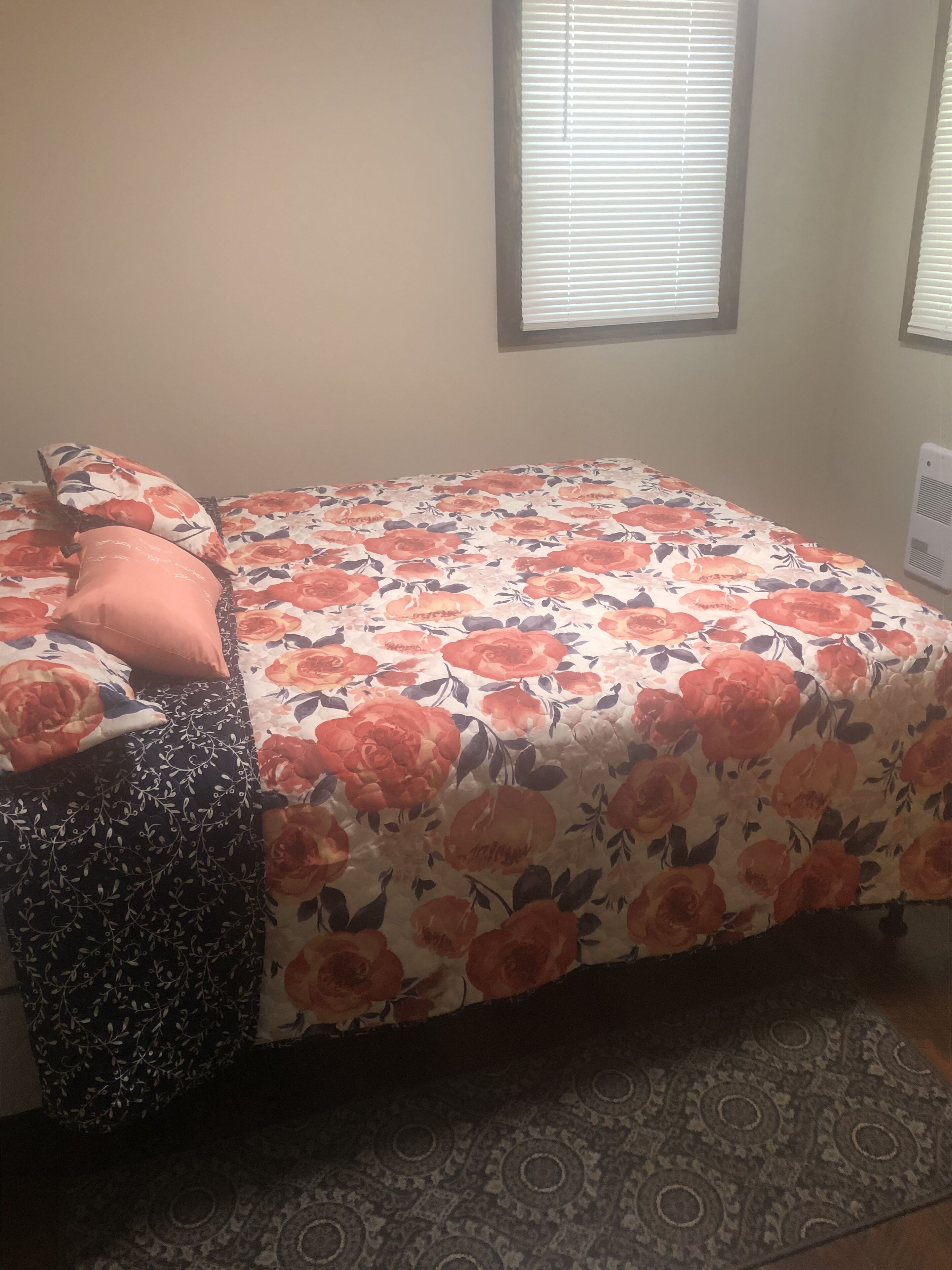 Un dormitorio con colcha estampada, un reposapiés negro con estampado y una alfombra decorada.