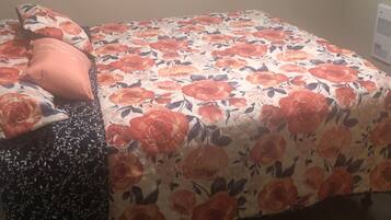 Un dormitorio con colcha estampada, un reposapiés negro con estampado y una alfombra decorada.