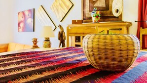 Ein Zimmer mit einem gewebten Korb auf einem farbenfrohen Teppich, einem Holztisch mit einer Lampe und gerahmten Kunstwerken an der Wand.