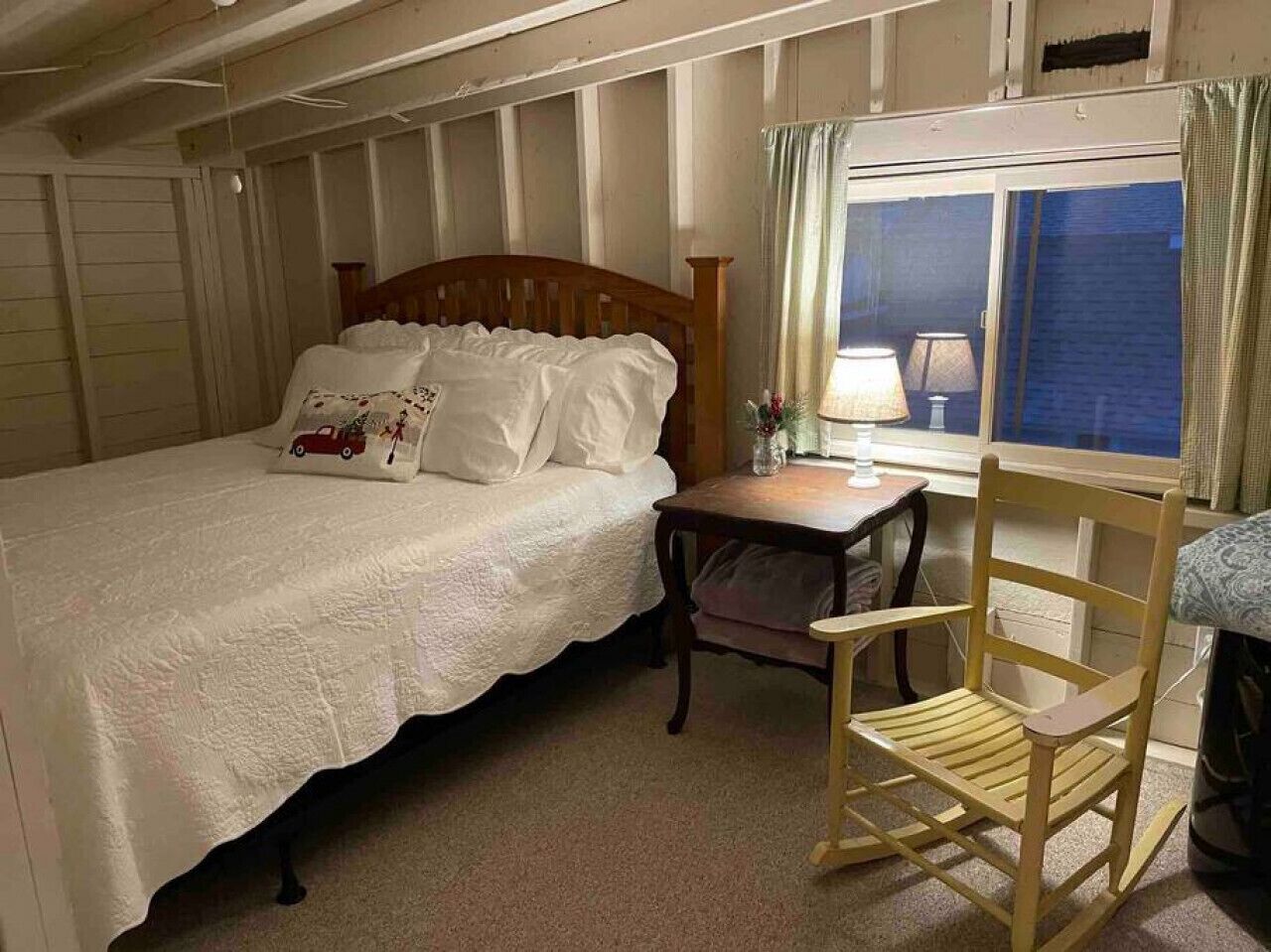 A bedroom with a single bed, a wooden chair, a small table, and a window with curtains.