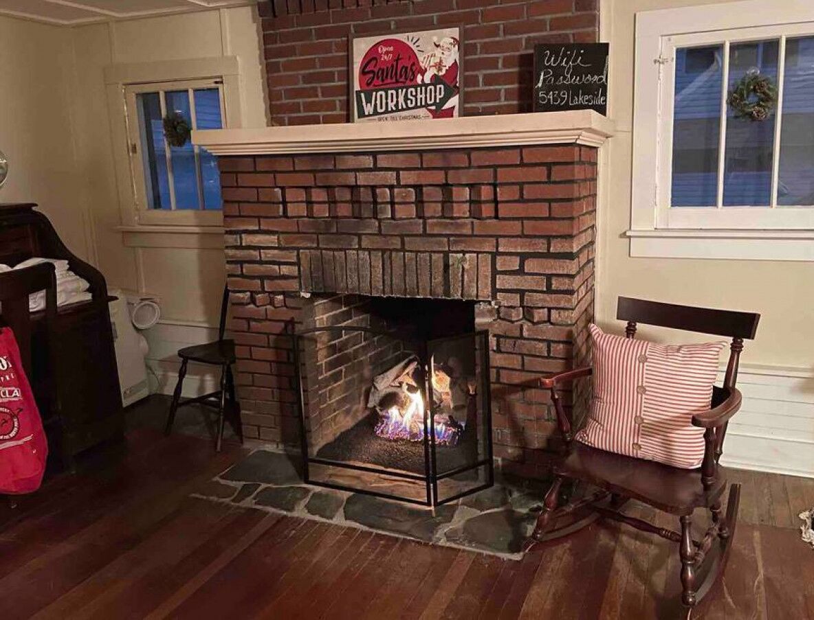 A fireplace with a brick surround, a sign above it, and a chair with striped cushions to the right.