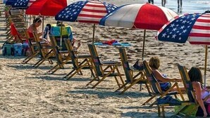 Beach chairs and umbrellas with American flags, people relaxing on the sand, and the ocean in the background. - Beautiful Beach House with Gulf views, 2 min walk to Beach!!  (Galveston)
