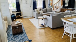 A spacious living room with a grey sofa, a wooden coffee table, and a TV on a wooden cabinet. There is a staircase with wooden railings leading to an upper level. - Beautiful Beach House with Gulf views, 2 min walk to Beach!!  (Galveston)