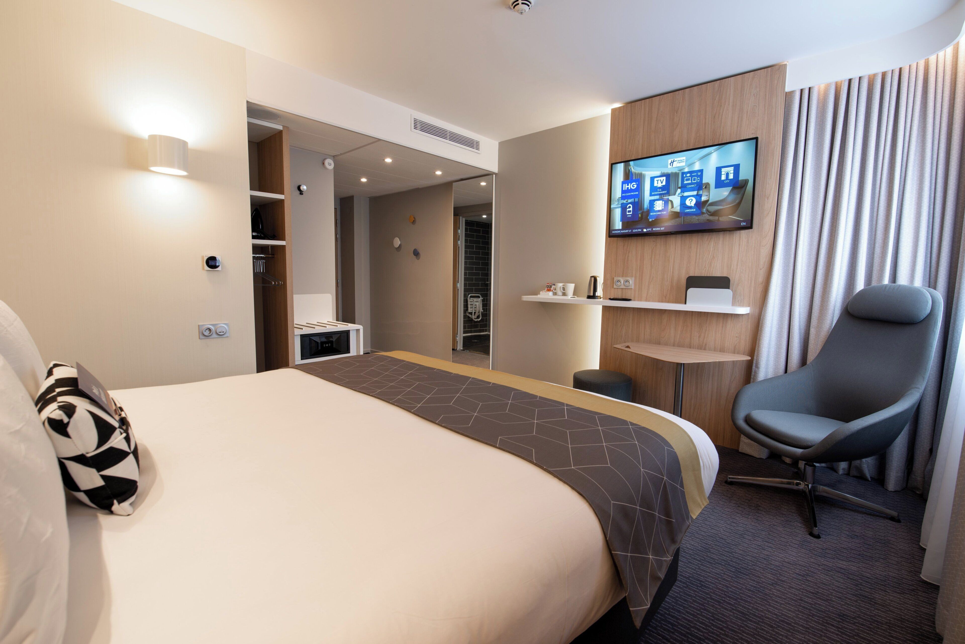A hotel room with a bed, a desk, a chair, a TV, and a bathroom.