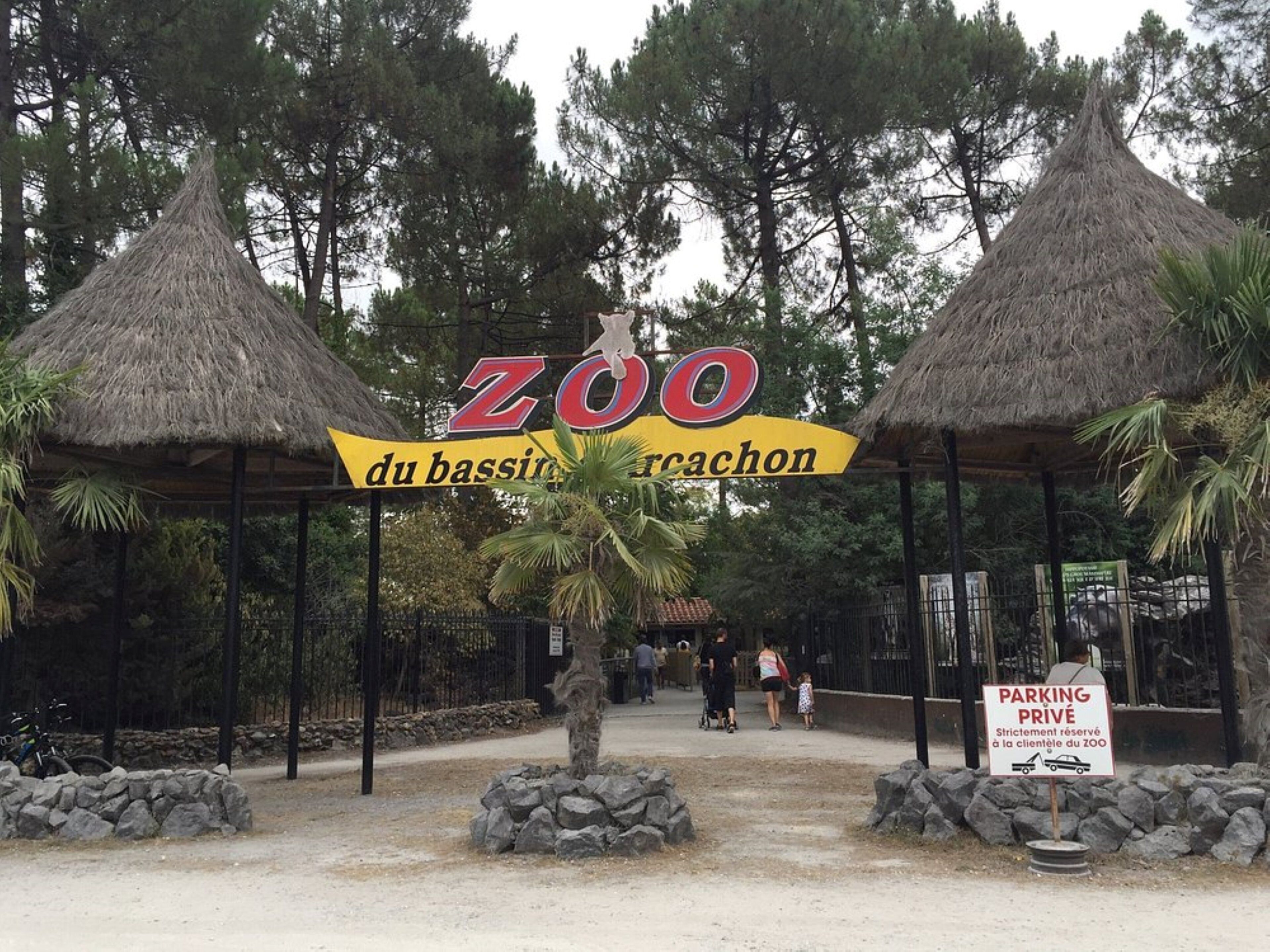 Entrada de un zoológico con estructuras de techo de paja y un cartel que indica estacionamiento privado.