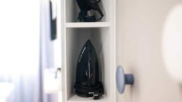 Un couloir étroit avec un mur blanc, une porte en bois et une étagère sur laquelle se trouvent une bouilloire et un fer à repasser.