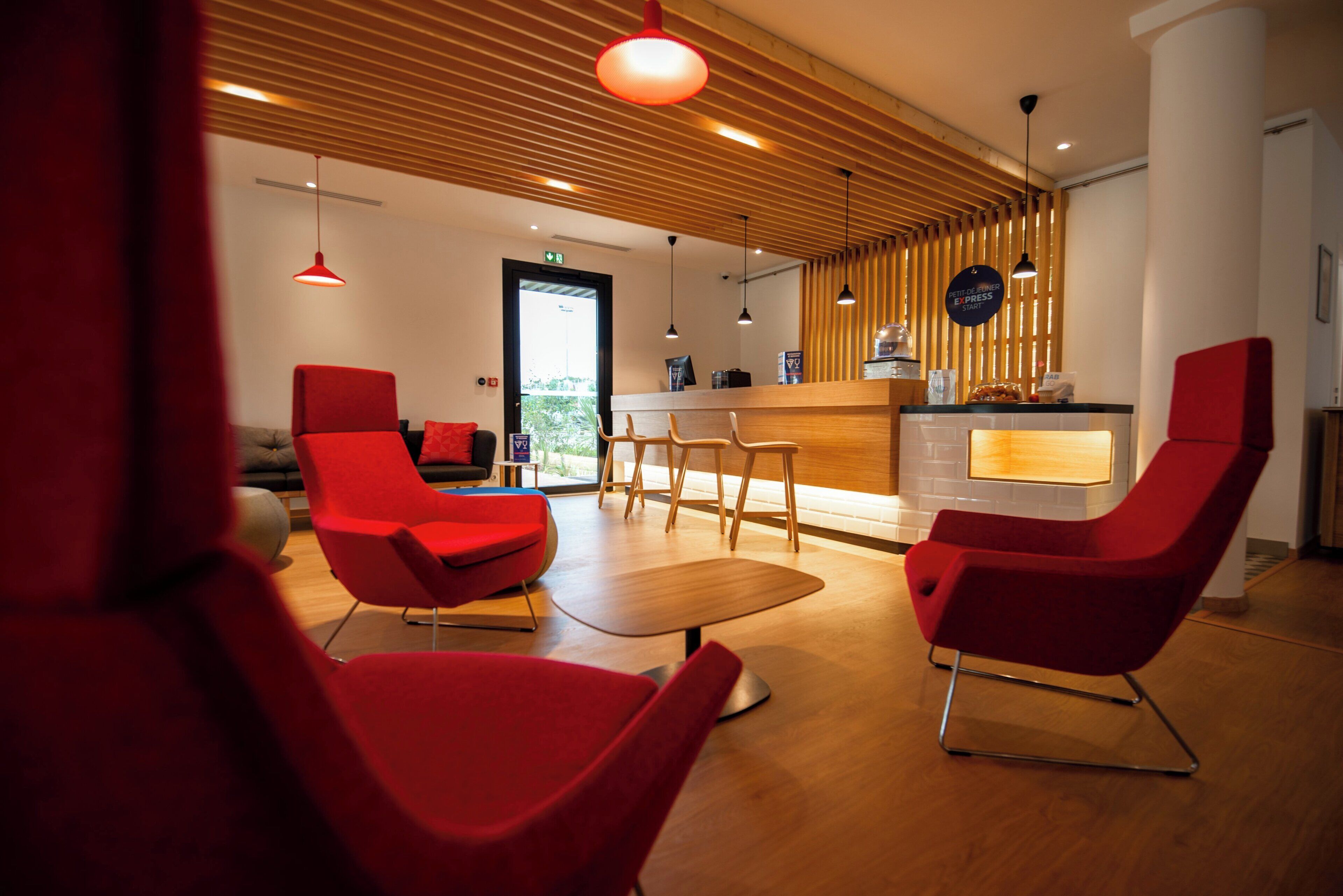 Un intérieur moderne avec des chaises rouges, une table en bois et un comptoir d’accueil.