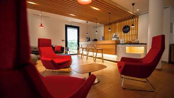 Un intérieur moderne avec des chaises rouges, une table en bois et un comptoir d’accueil.