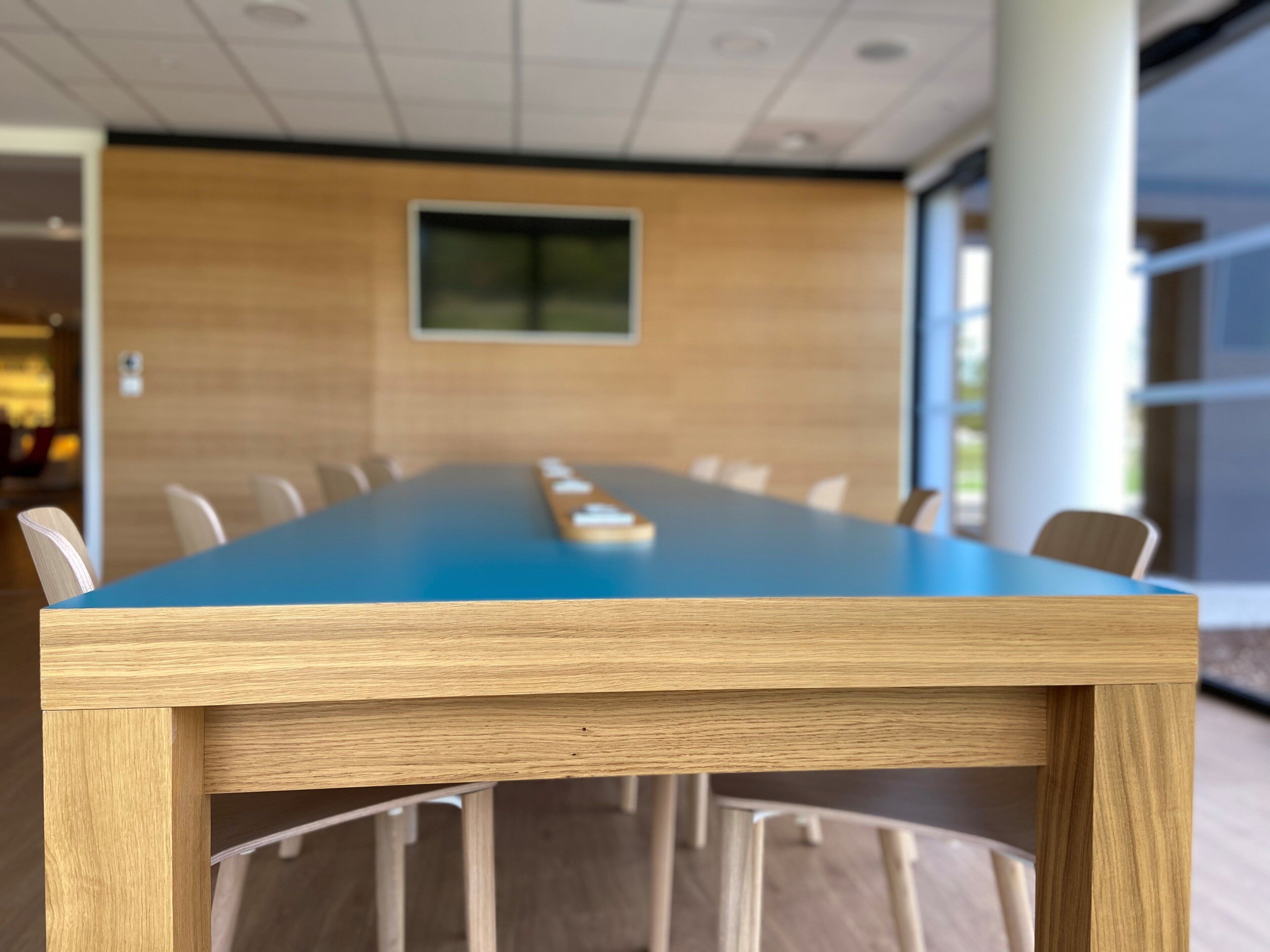 A conference table with chairs, a wooden panel wall, and a window.