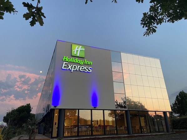 A Holiday Inn Express building with a modern glass facade, large windows, and a visible interior with seating arrangements. - Holiday Inn Express Arcachon - La Teste by IHG (La Teste-de-Buch)