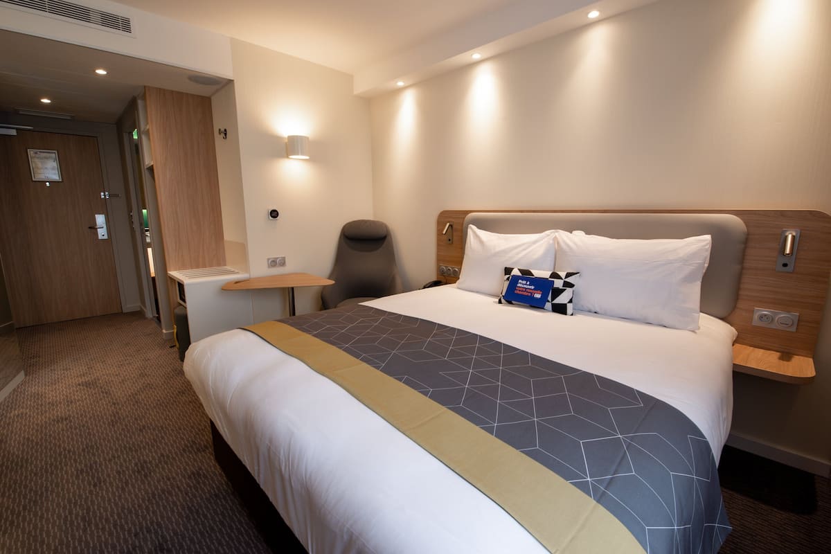Une chambre d’hôtel avec un grand lit, une table de chevet, une chaise, un bureau et une porte.